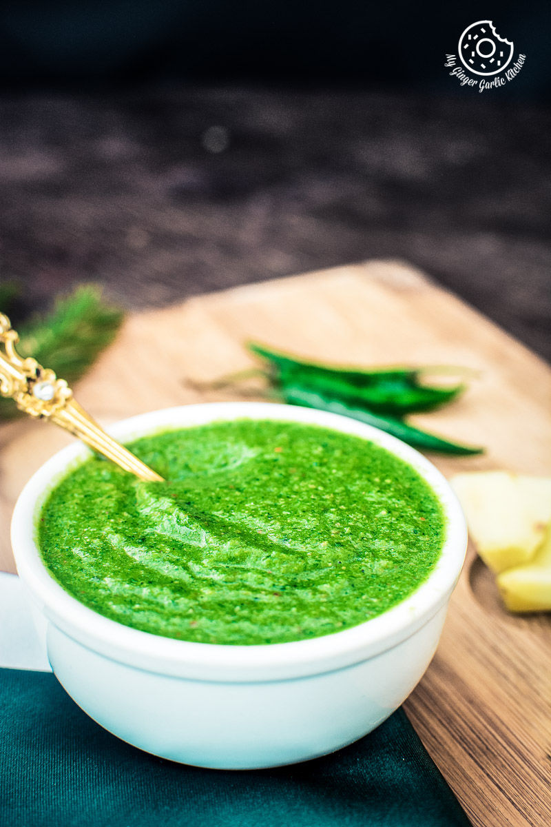 there is a bowl of green coriander chutney with a gold spoon in it