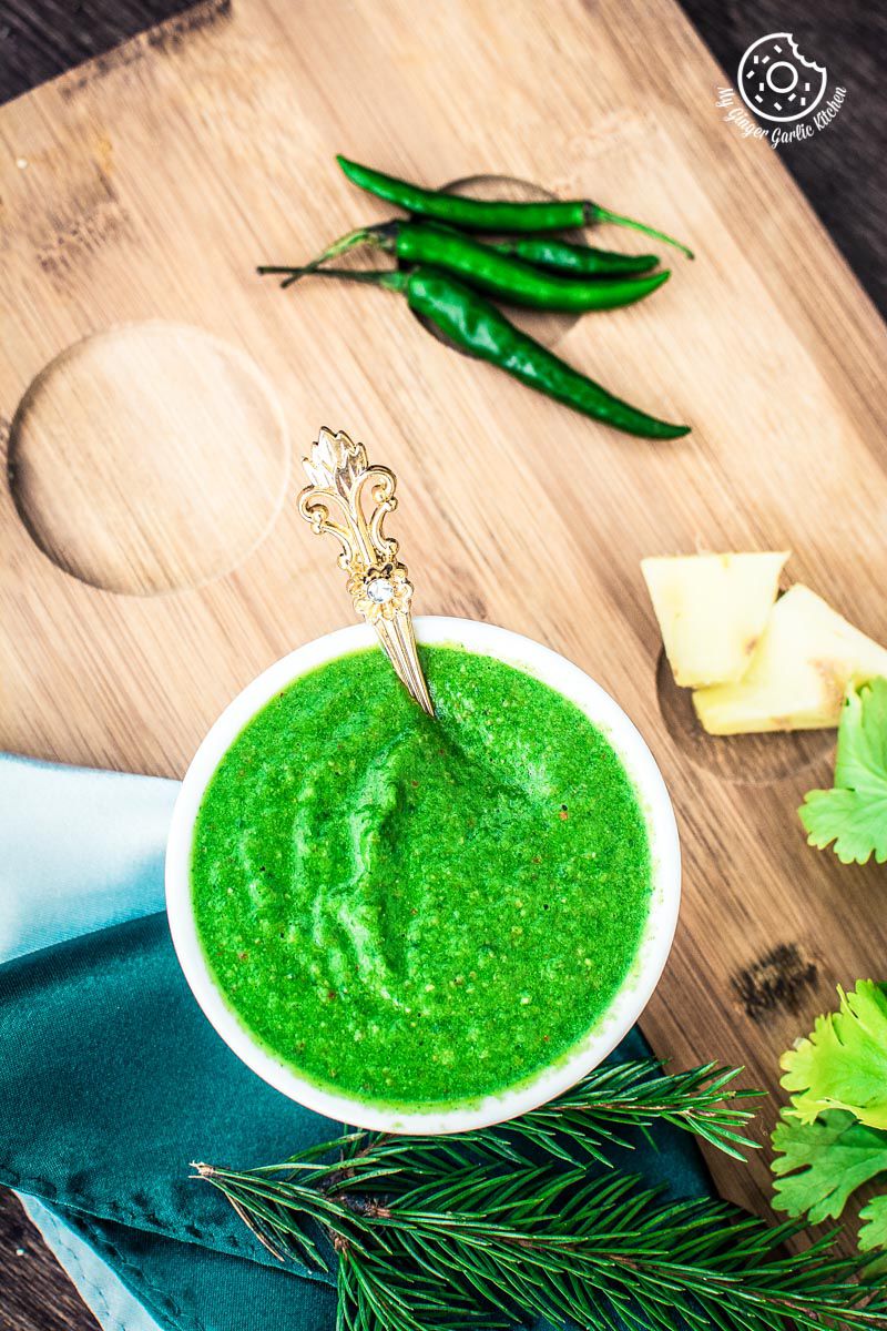 there is a bowl of green coriander chutney with a spoon in it