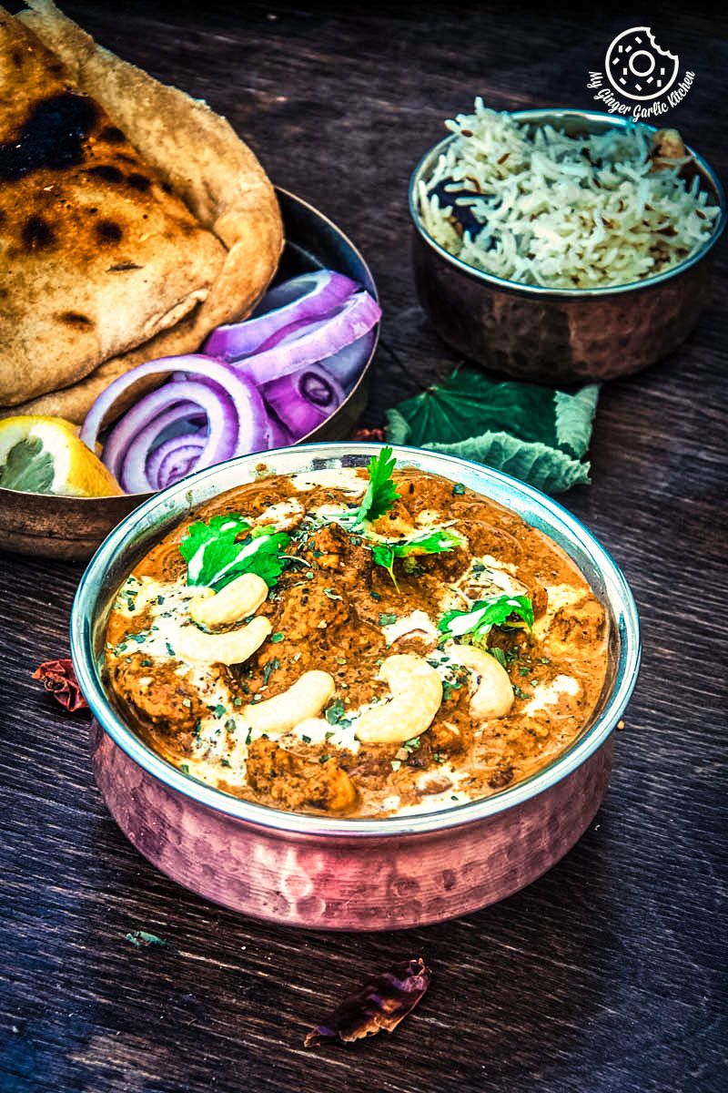 a bowl of restaurant style shahi kaju curry with some naan and salad