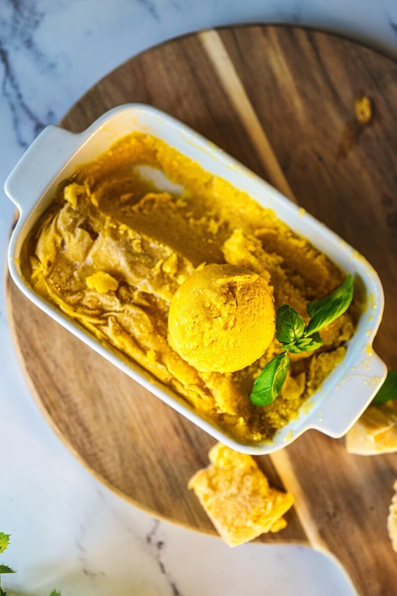 Homemade 3 ingredient mango sorbet in a white dish, scooped and ready to serve, with fresh basil garnish