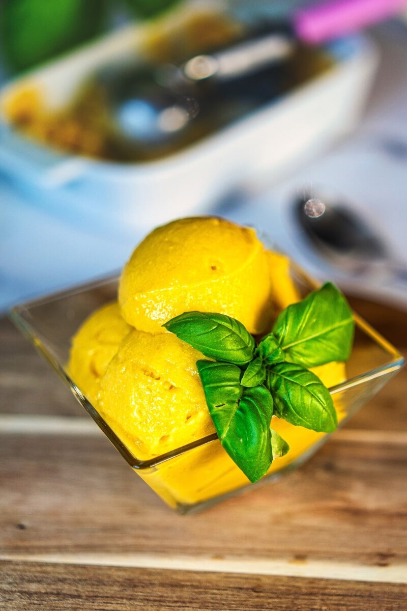 Refreshing 3 ingredient mango sorbet in a glass bowl, garnished with basil leaves on a wooden surface