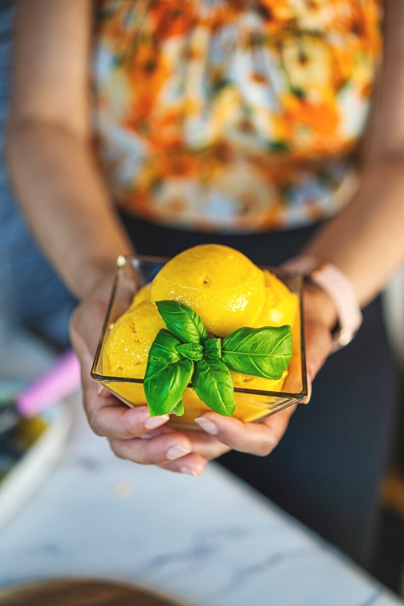 Woman holding a bowl of three-ingredient mango sorbet, topped with vibrant basil leaves