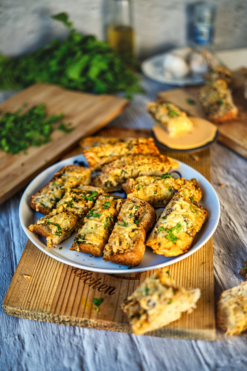 Gourmet cheese-crusted garlic bread platter with fresh herbs and olive oil on rustic wooden board