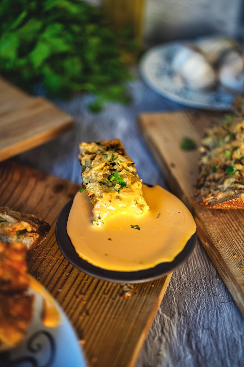 Close-up of golden garlic bread slice dipped in creamy sauce on wooden surface with dramatic lighting