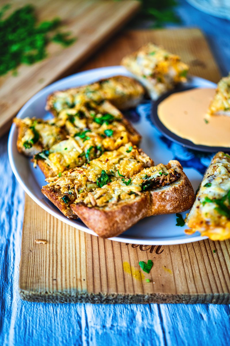 Homemade cheesy garlic bread topped with fresh herbs served on rustic wooden board with dipping sauce