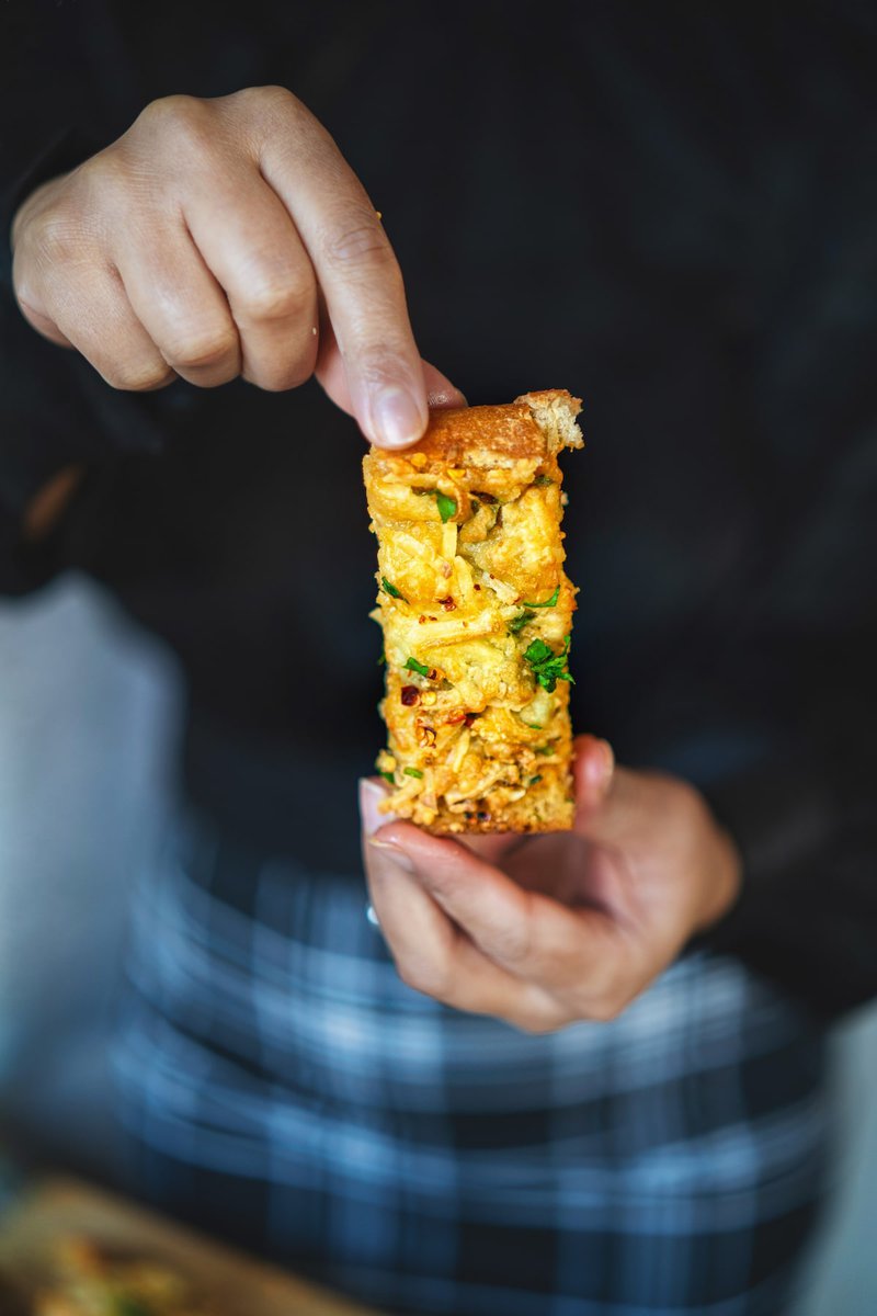 Hand holding a slice of cheesy bread topped with herbs