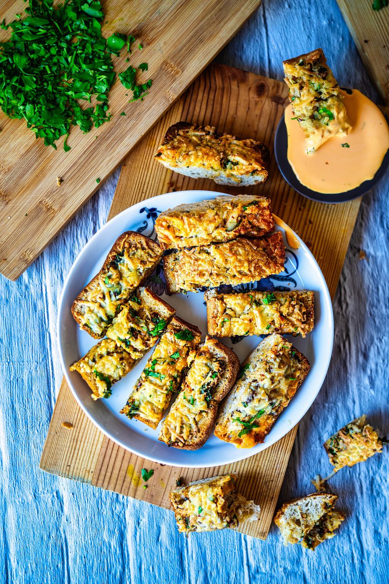 Overhead view of artisanal garlic bread slices garnished with parsley and served with creamy dipping sauce on blue tablecloth