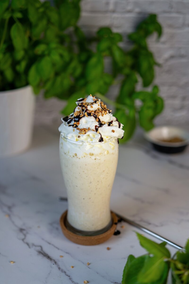 Frosty banana milkshake with whipped cream, chocolate drizzle, and nut topping in a clear glass, easy homemade milkshake recipe.