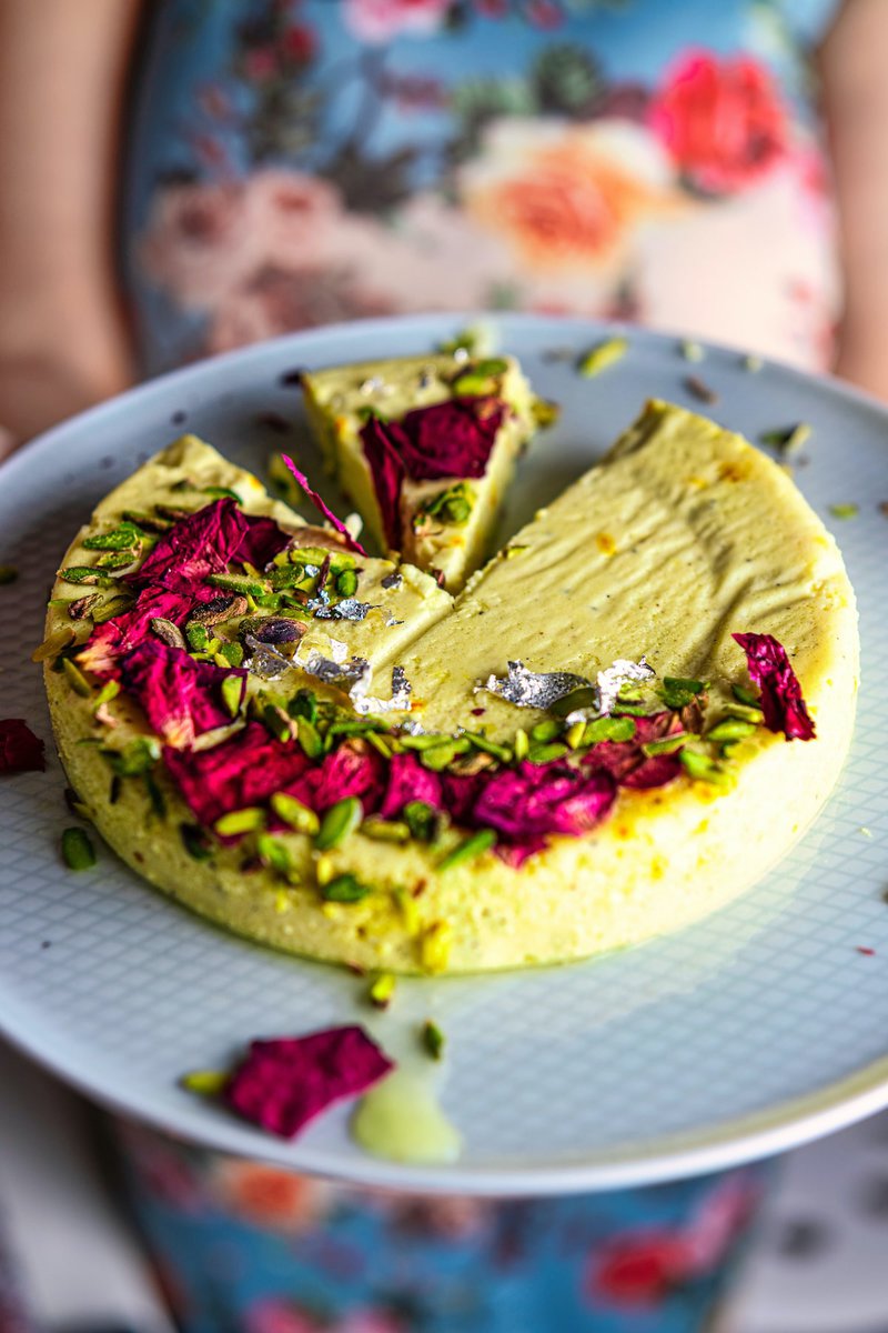 A  a plate of bhapa doi, a Bengali dessert made from steamed yogurt held by a person with a floral dress, garnished with pistachios and rose petals.