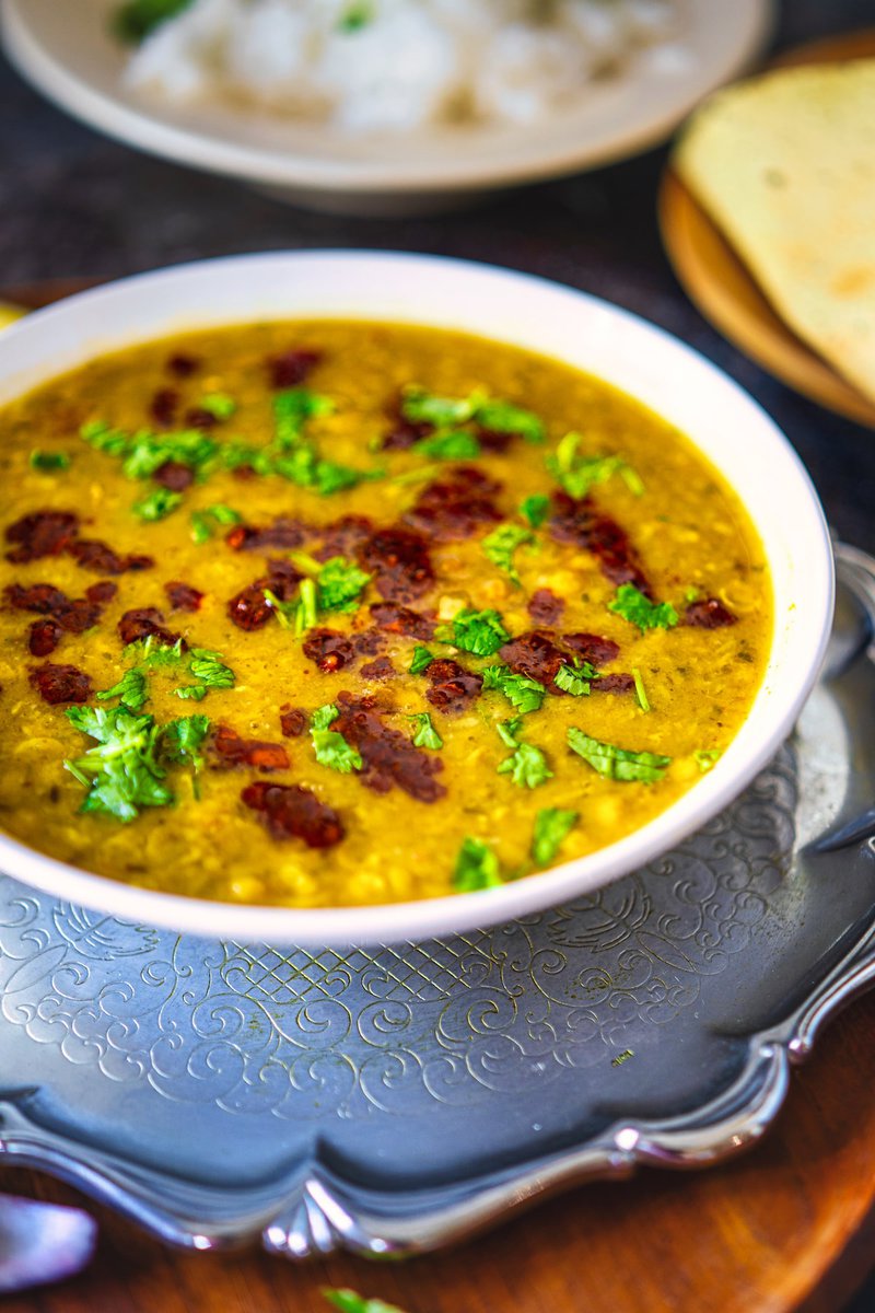 Close-up of a bowl of chana dal garnished with cilantro and red chili tempering, served on a silver platter with a side of rice and a papad.