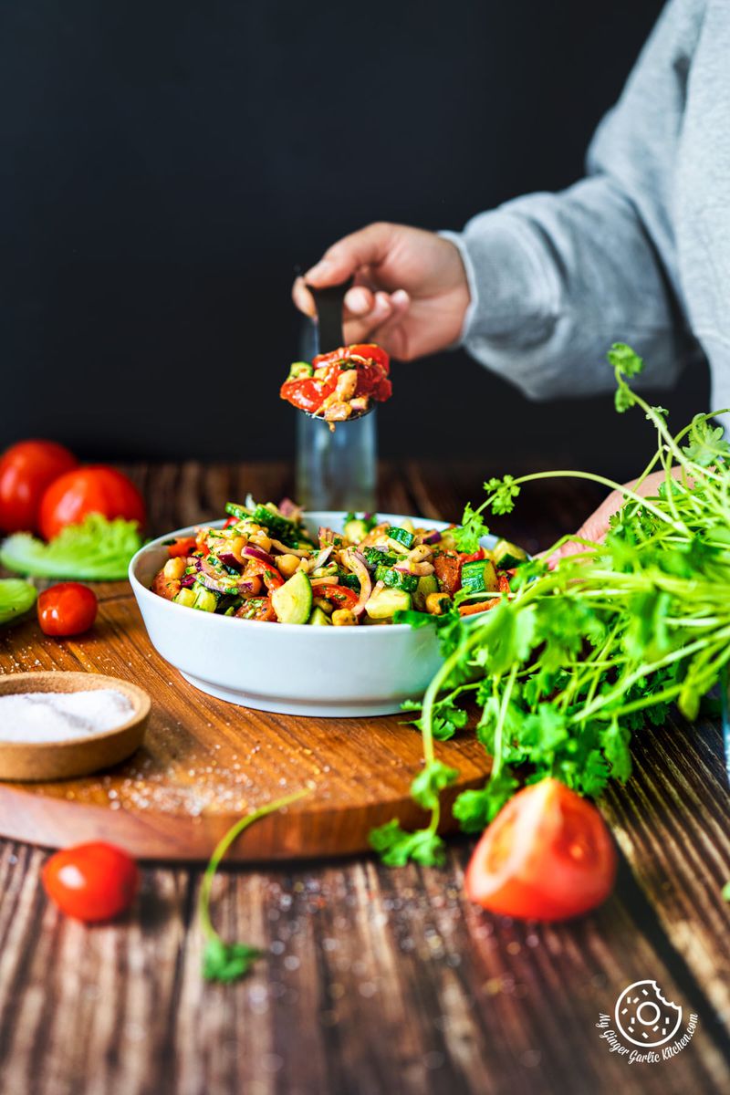 a hand holding a black spoon filled with chickpea salad over the chickpea salad bowl