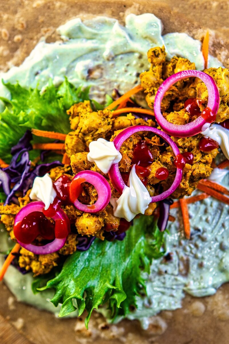 Close-up of spicy chickpea tikka filling, vibrant lettuce, carrots, red onions, and creamy sauces on whole wheat flatbread for vegan wrap recipe