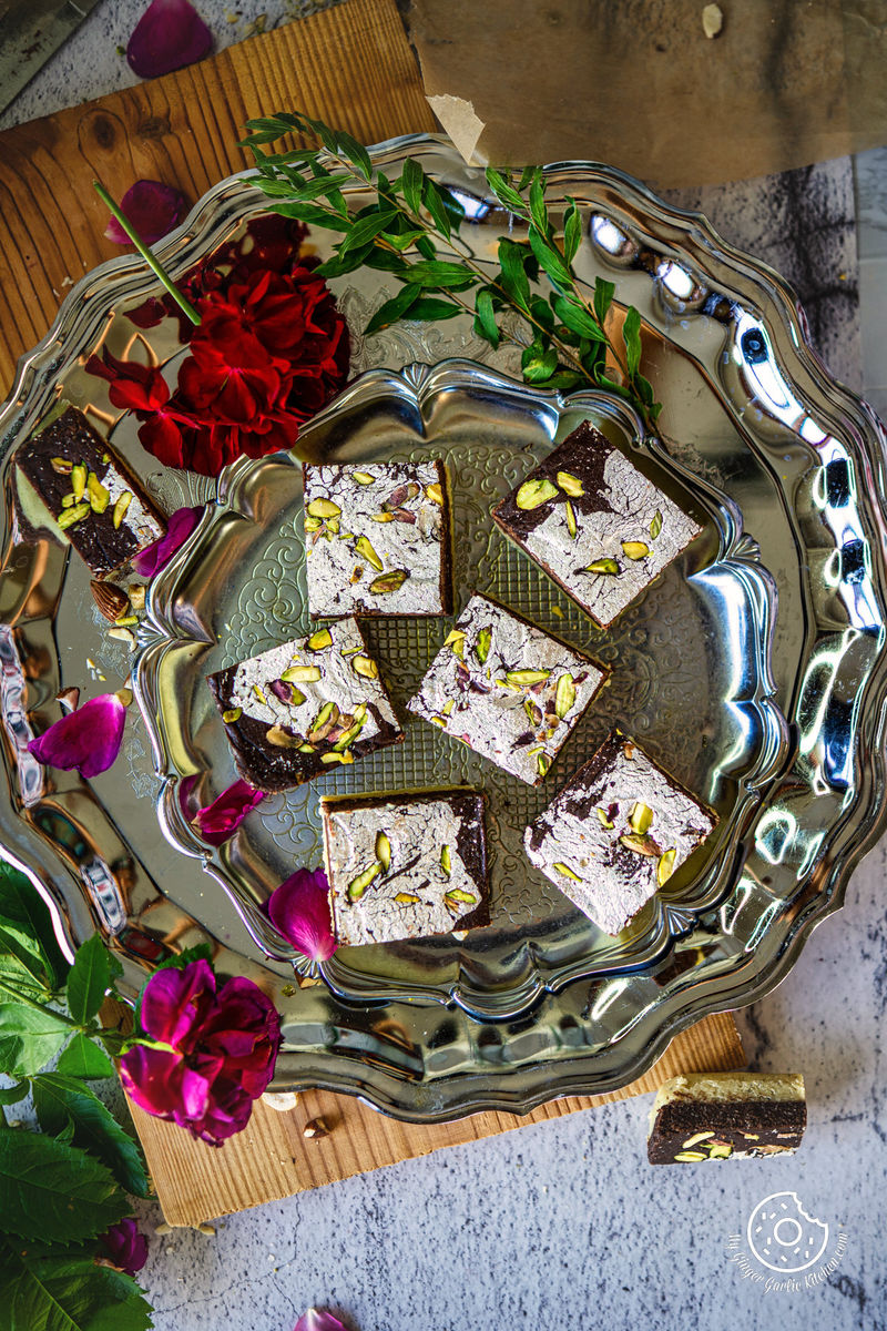 overhead shot ot six chocolate burfis in a metal plate  with rose flowers on the side