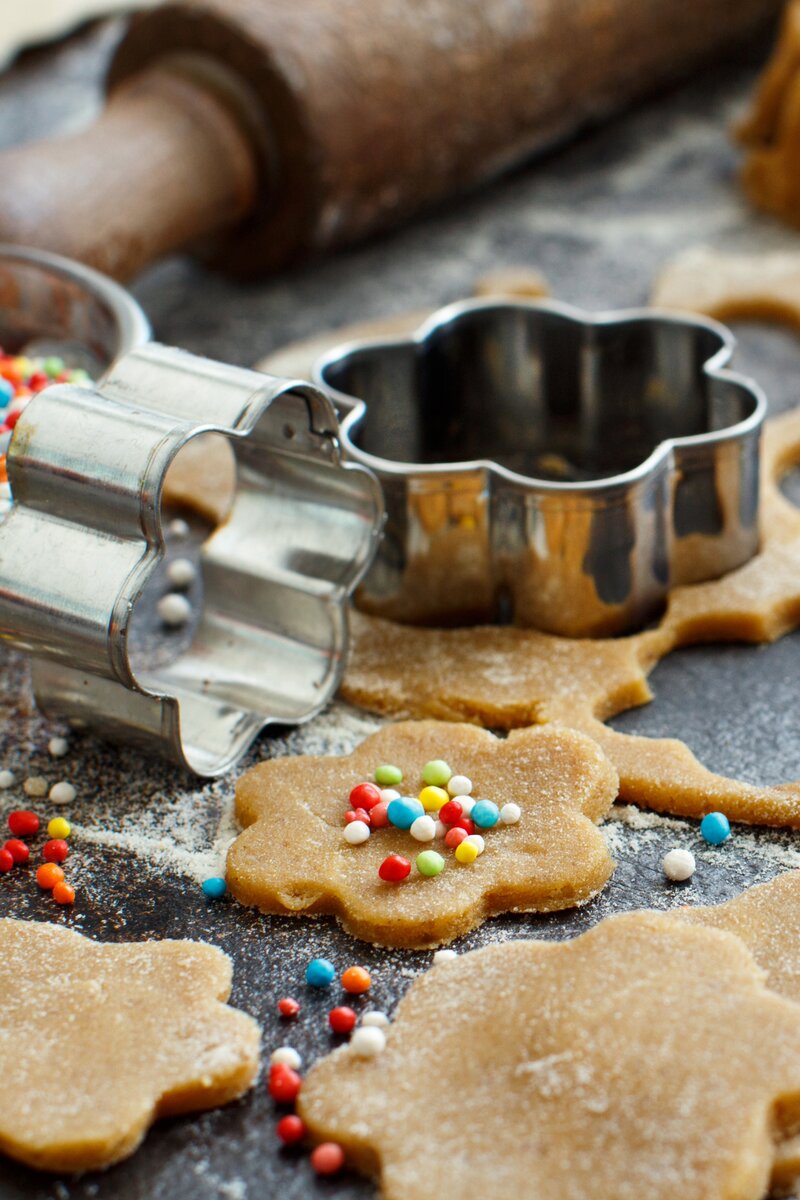 Flower-shaped cookie dough cutouts with colorful sprinkles and metal cookie cutters, holiday baking scene.