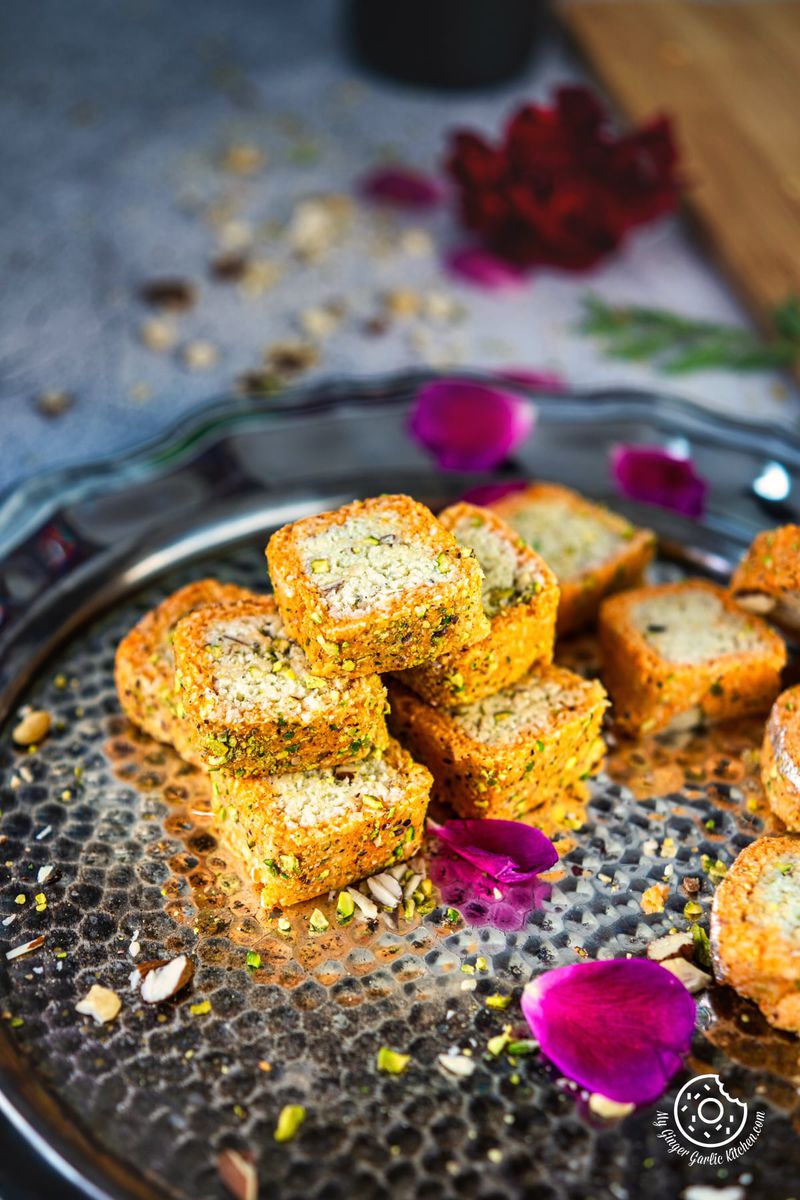 coconut burfi roll stack on a metal plate with rose petals