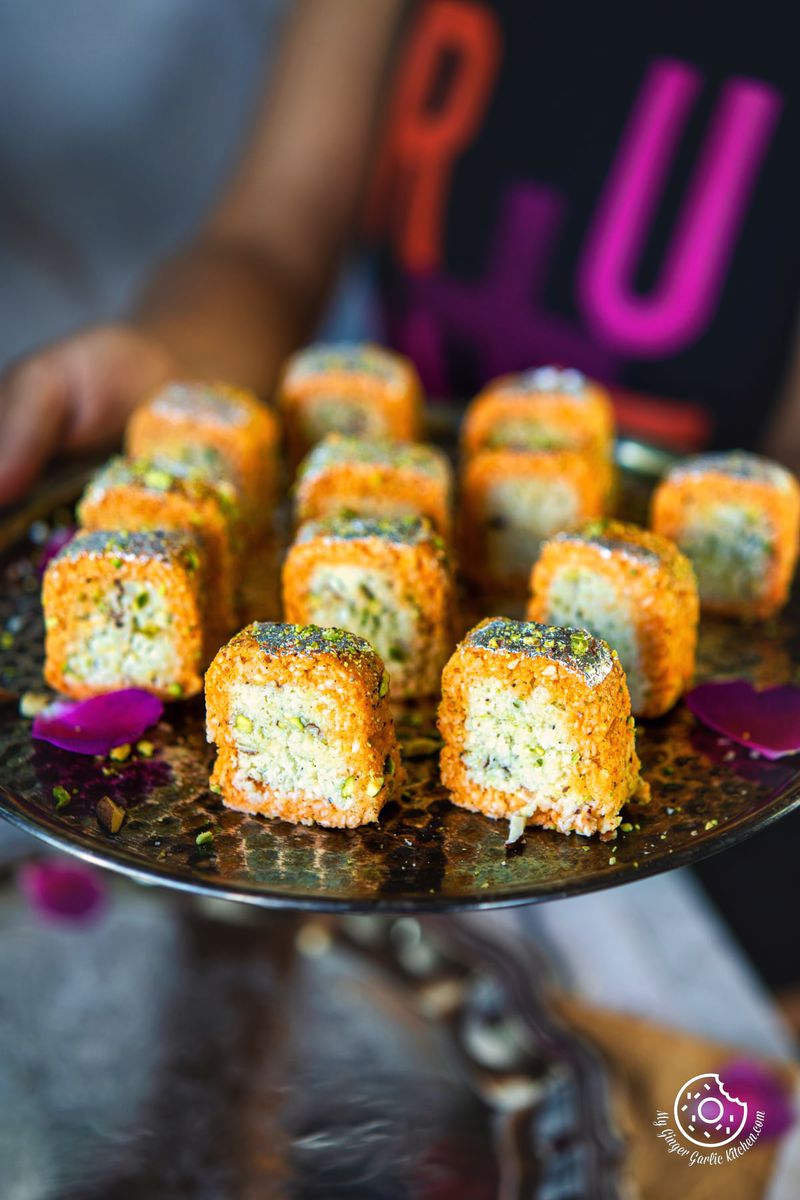 a female holding a metal plate filled with twelve coconut burfi rolls