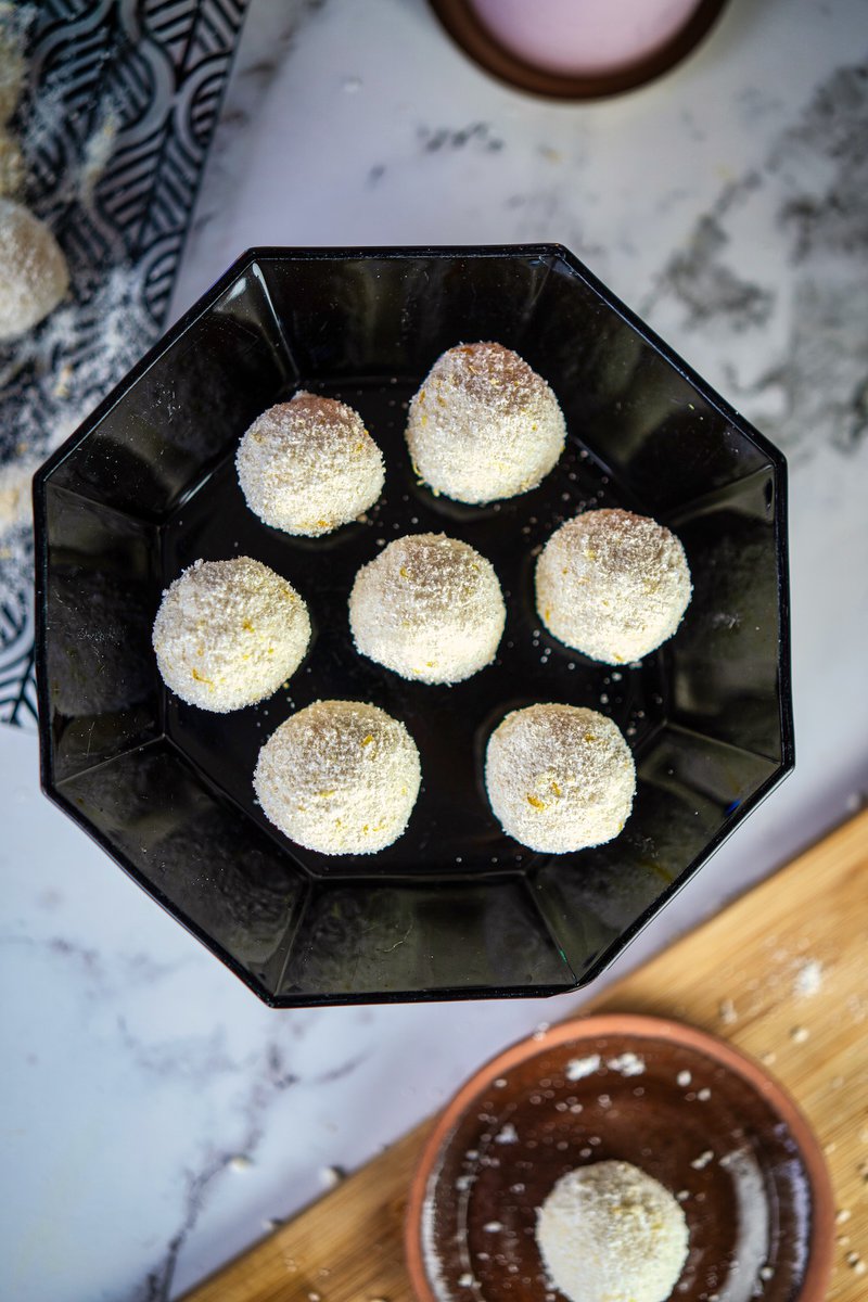 Overhead view of seven white cottage cheese lemon balls arranged on a black octagonal plate against a marble surface