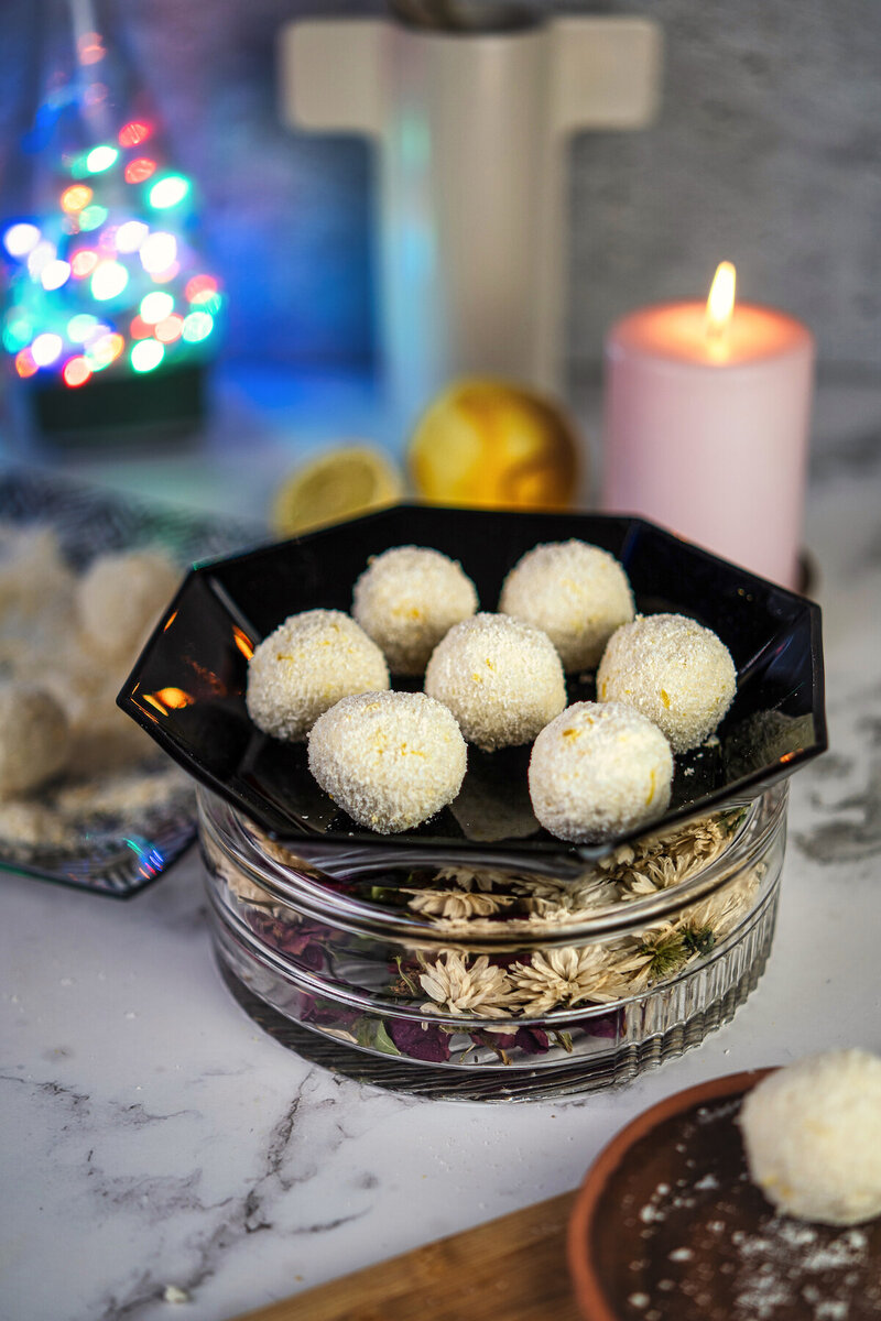A black dish filled with high protein cottage cheese lemon balls, surrounded by candles and decorative lights in a stylish setting.