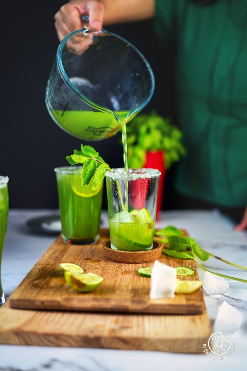 a female pouring cucumber cooler in a transparent glass