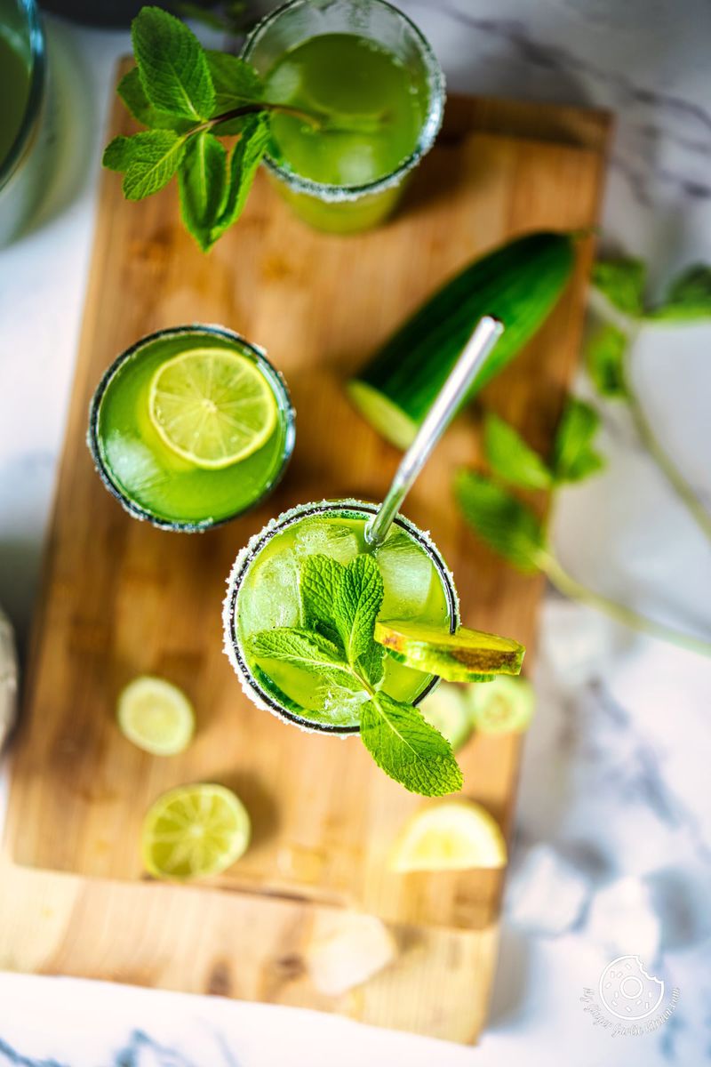 overhead shot of cucumber cooler served in three glasses with some lime slices and ice cubes on the side