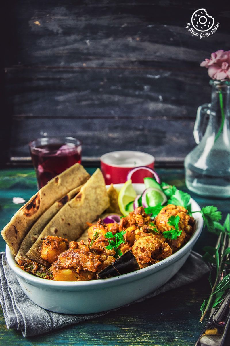 there is a bowl of a dhaba style dry aloo gobi with a paratha, onions, a bowl of yogurt, and a glass of tea