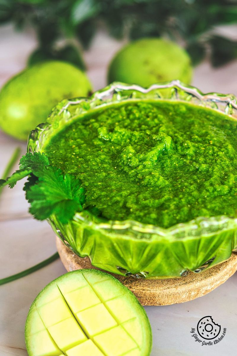 closeup photo of a bowl of green sauce with a slice of unripe mango next to it