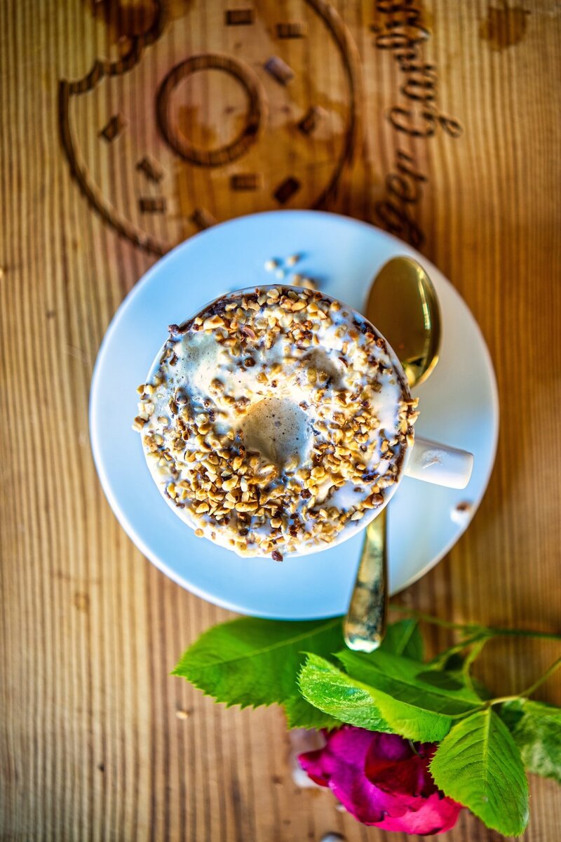 Overhead view of hazelnut affogato coffee dessert with creamy ice cream and roasted hazelnut topping beside gold spoon and red rose on wooden table