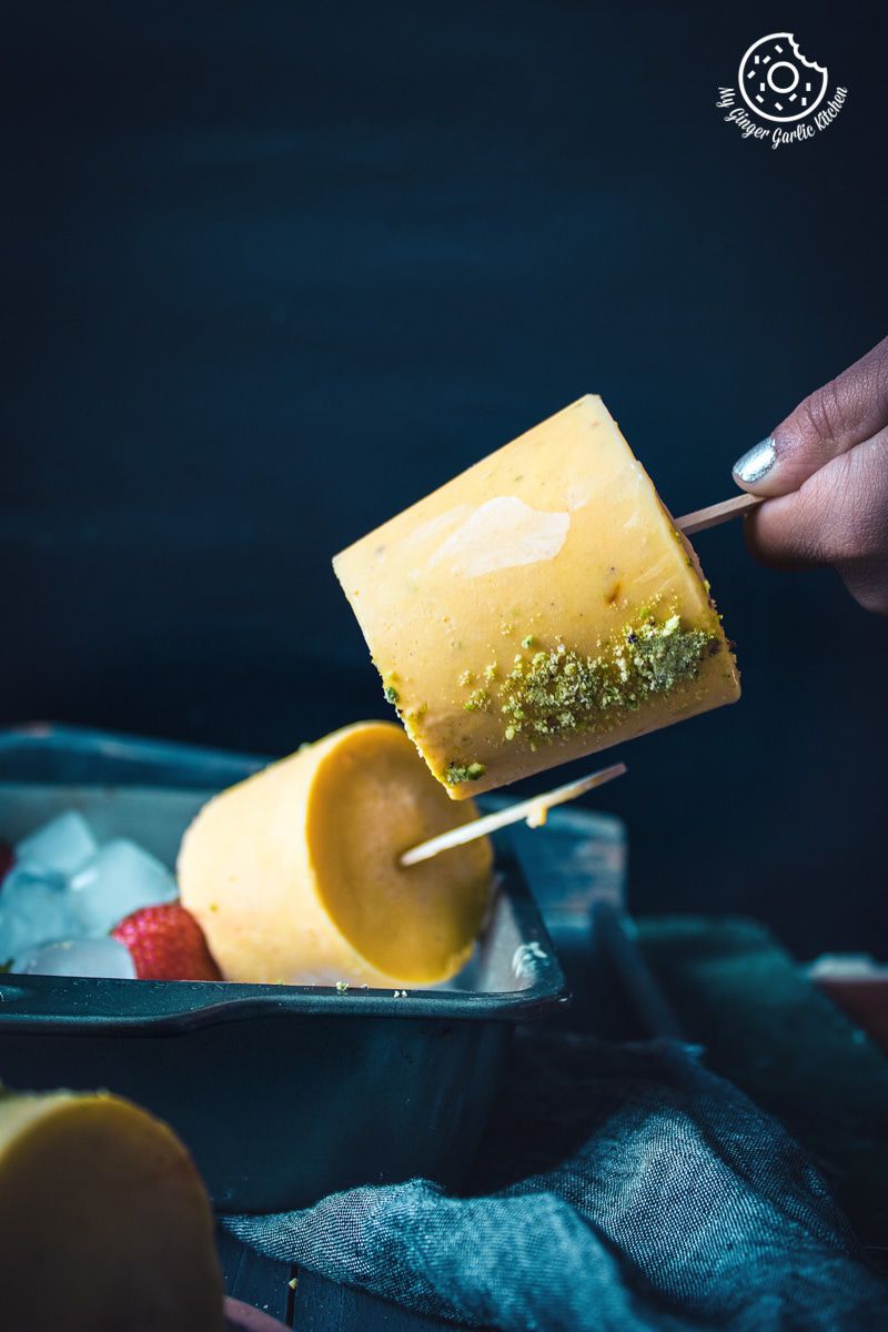 someone is holding a mango kulfi popsicle