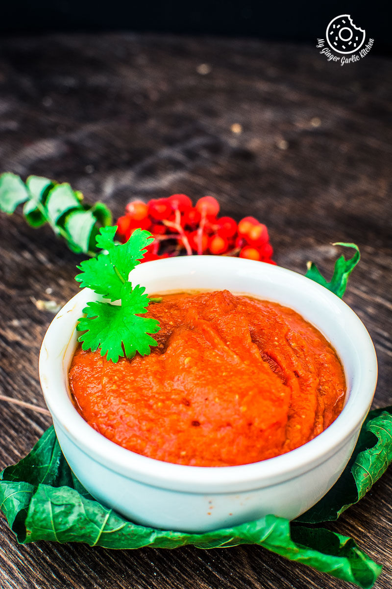there is a bowl of red chutney or rajasthani lehsun ki chutney with a sprig of cilantro