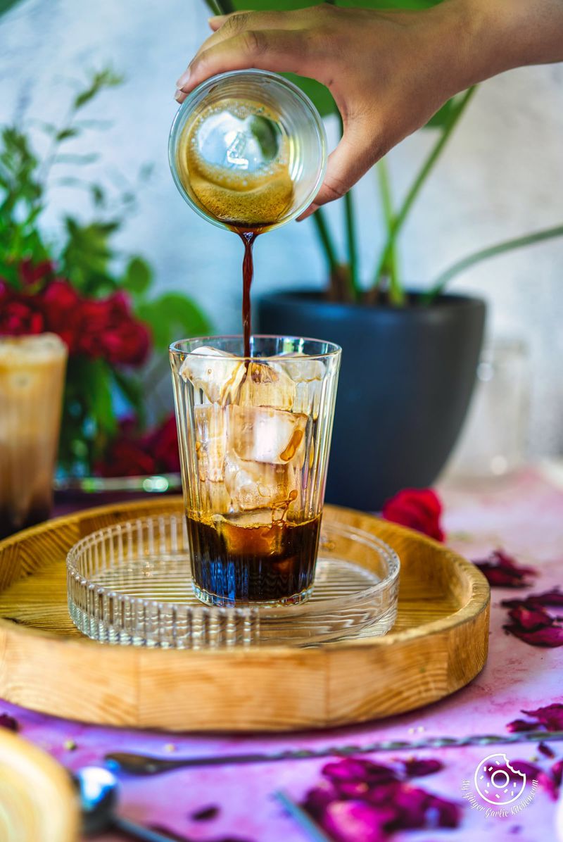 Picture of the iced rose latte. A hand is pouring coffee into the glass.