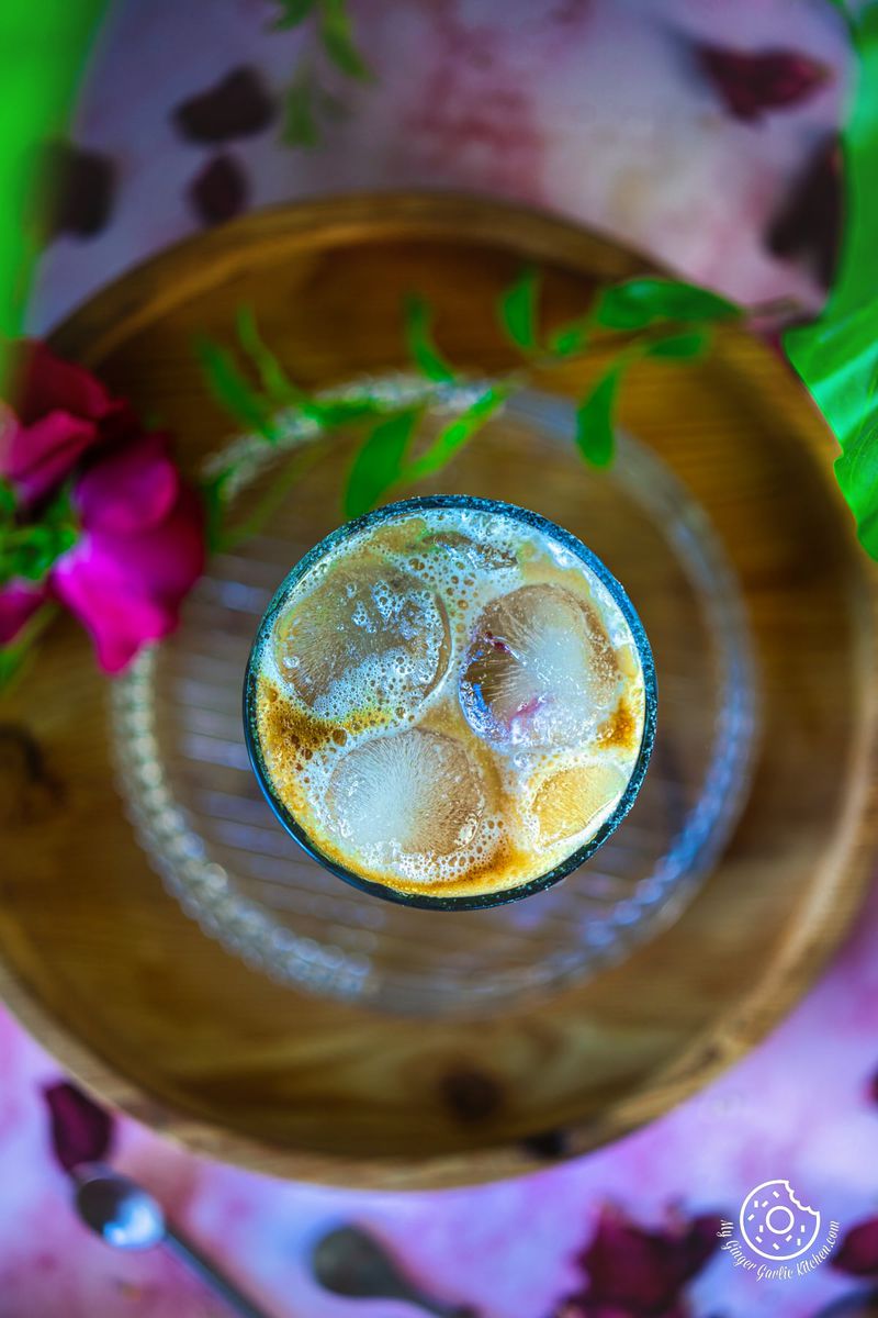 Overhead view of rose flavoured iced latte with some rose petals on the side.