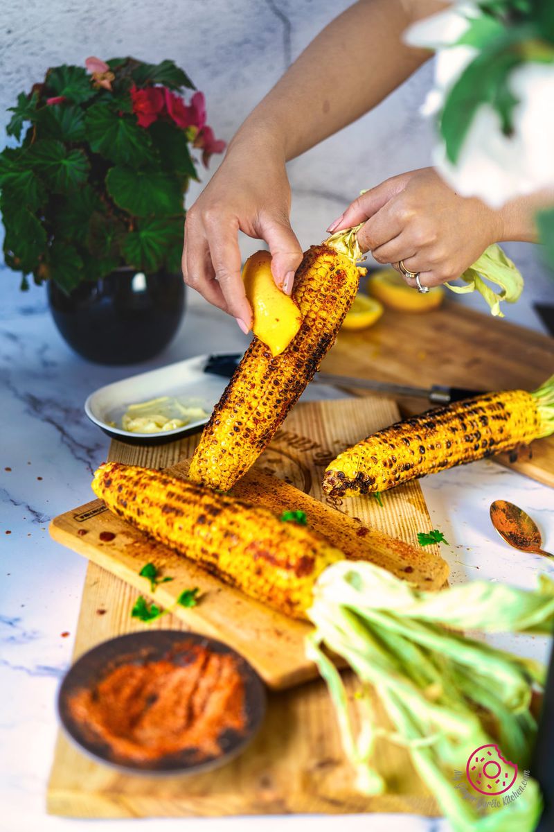 a hand rubbing lemon slice over indian roasted corn on the cob - masala bhutta