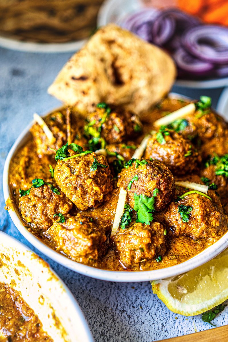 Restaurant style lauki kofta curry with roti, red onions and lemon, vegetarian Indian main course served in white bowl with fresh cilantro garnish