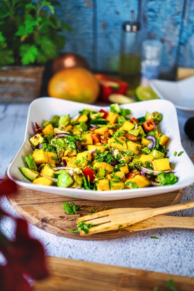 Fresh mango avocado salad with red onion cucumber and cilantro in white bowl on rustic wooden table healthy summer vegan recipe