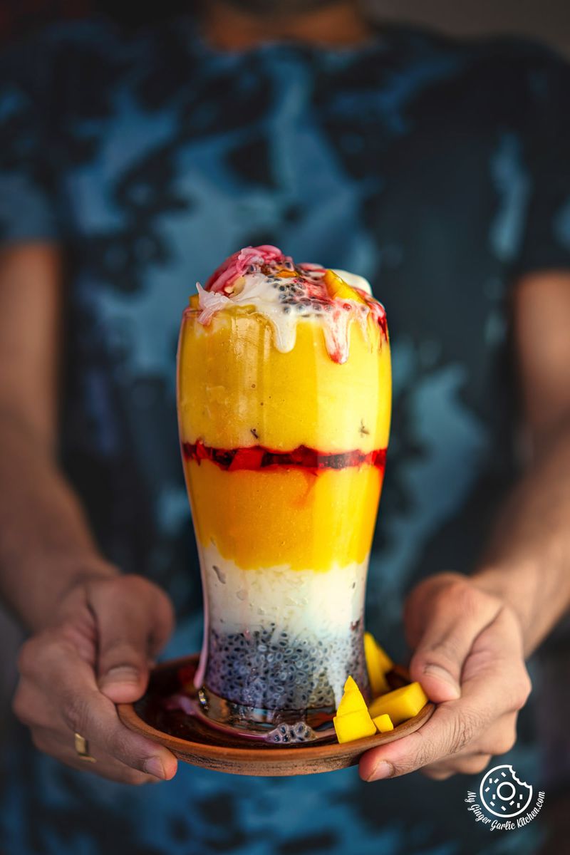 photo of a man holding a plate with a mango falooda dessert on it