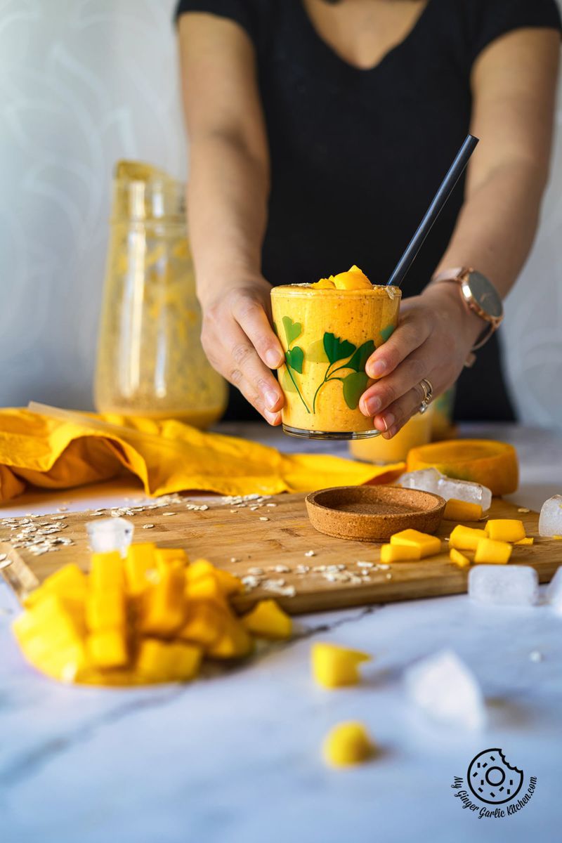 a female holding a glass of mango oat smoothie