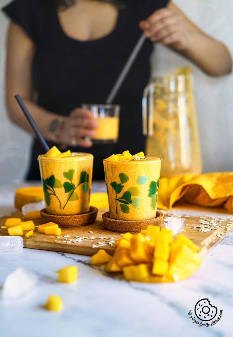  two glasses of mango oats smoothie with a female holding a glass of mango oat smoothie