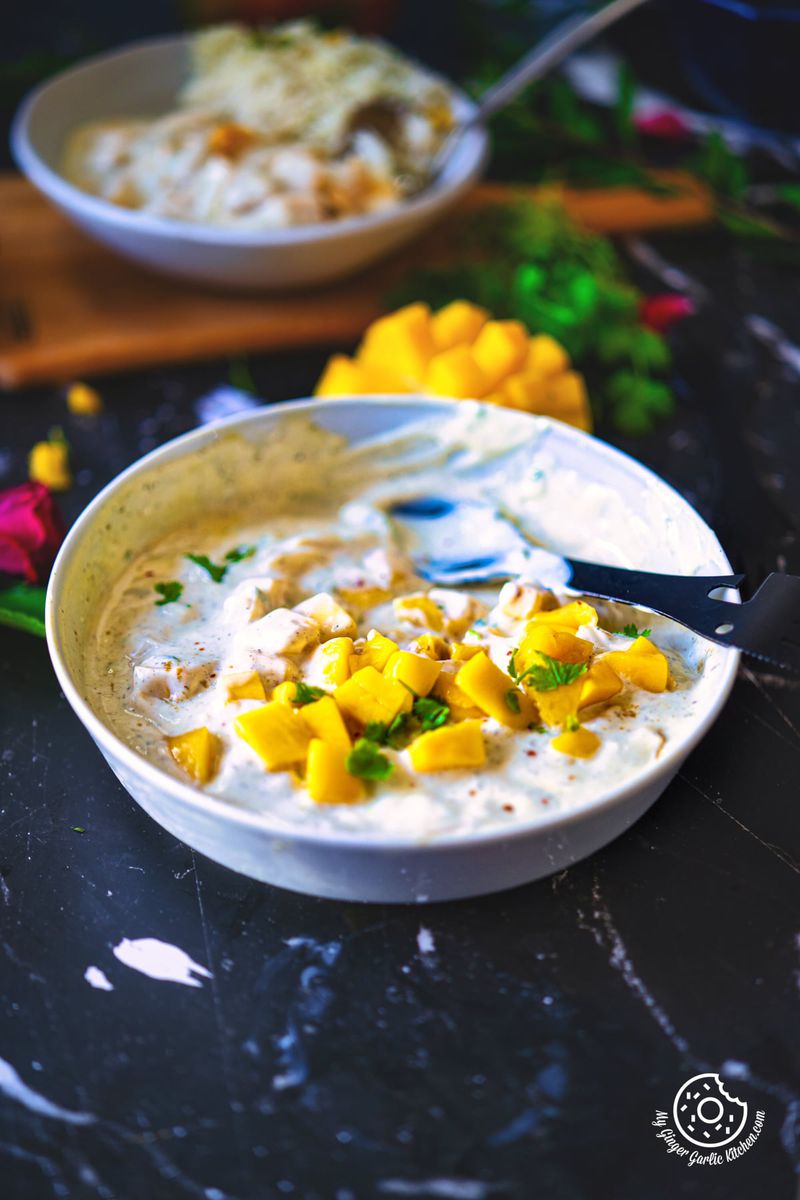 closeup shot of mango raita served in a grey bowl and garnished with mango chunks