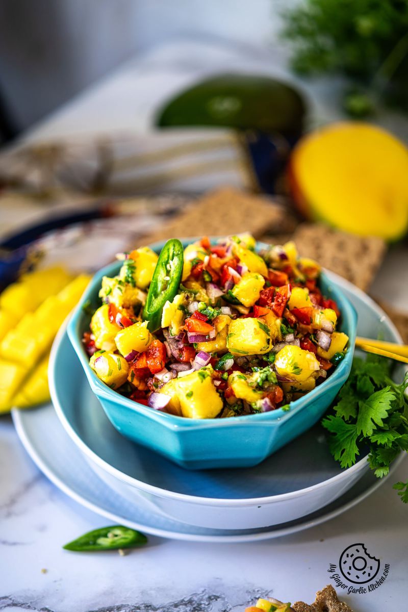 a blue bowl of mango salsa kept on a white marble background