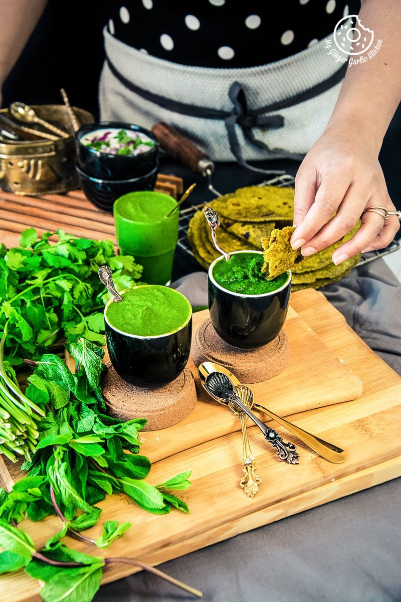 a female dipping flatbread into mint coriander chutneys served in a black ceramic bowl