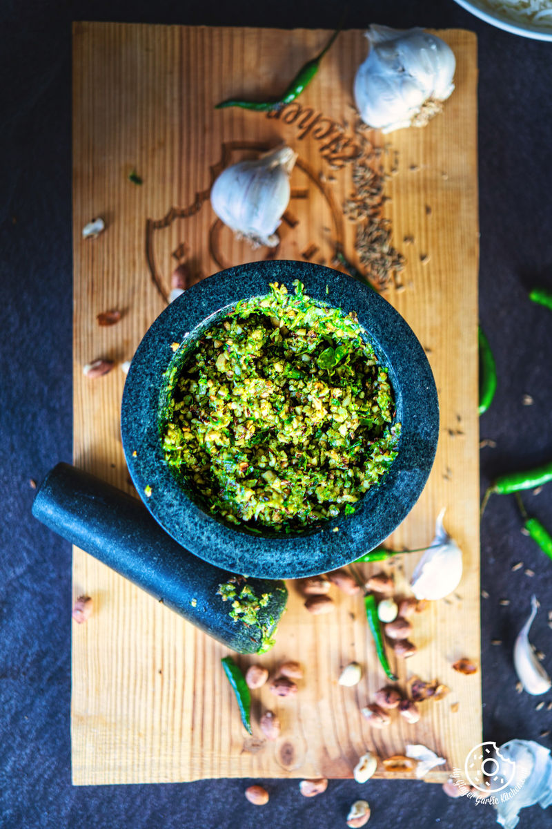 overhead shot of mortar with mirchi ka thecha with pestle, garlic, green chilies, and peanuts on the side 