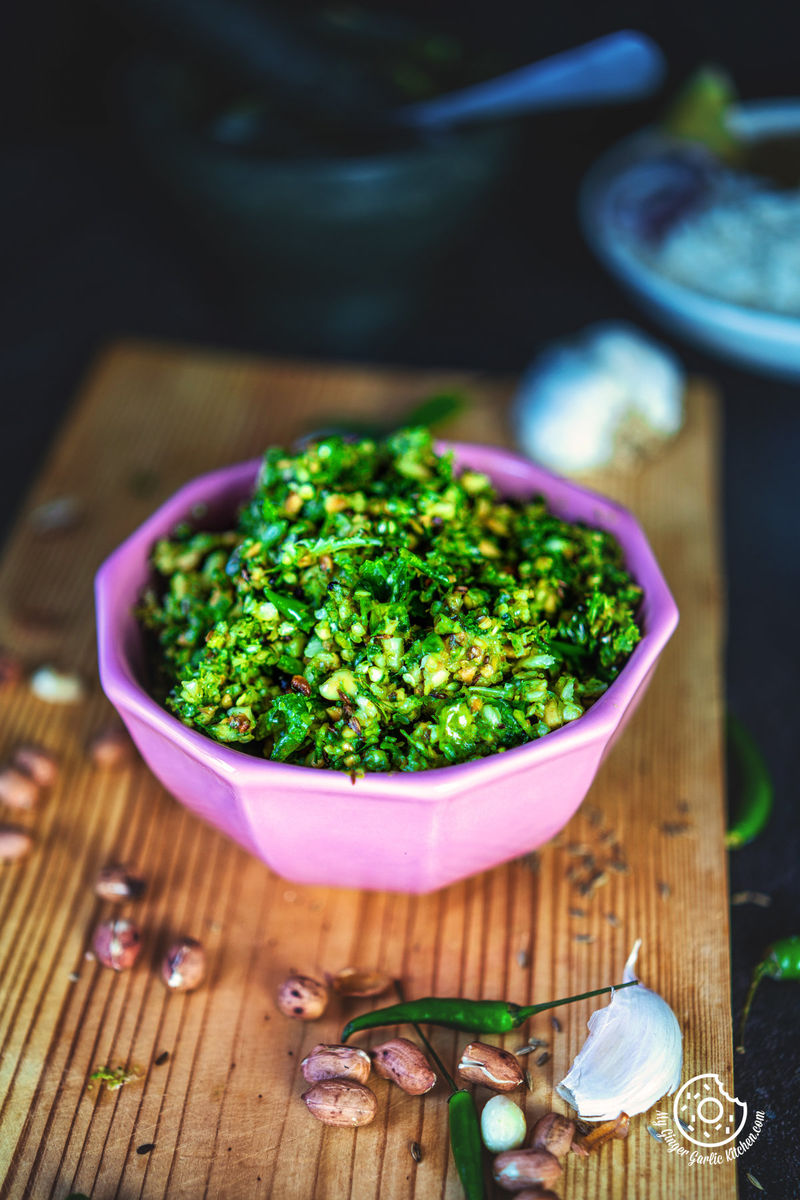 a pink bowl of mirchi ka thecha with garlic cloves and peanuts on side