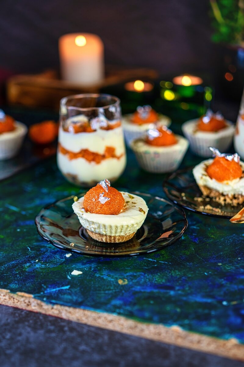 Close-up of mini no bake motichoor cheesecake with biscuit base and ladoo garnish, set against a deep blue tabletop