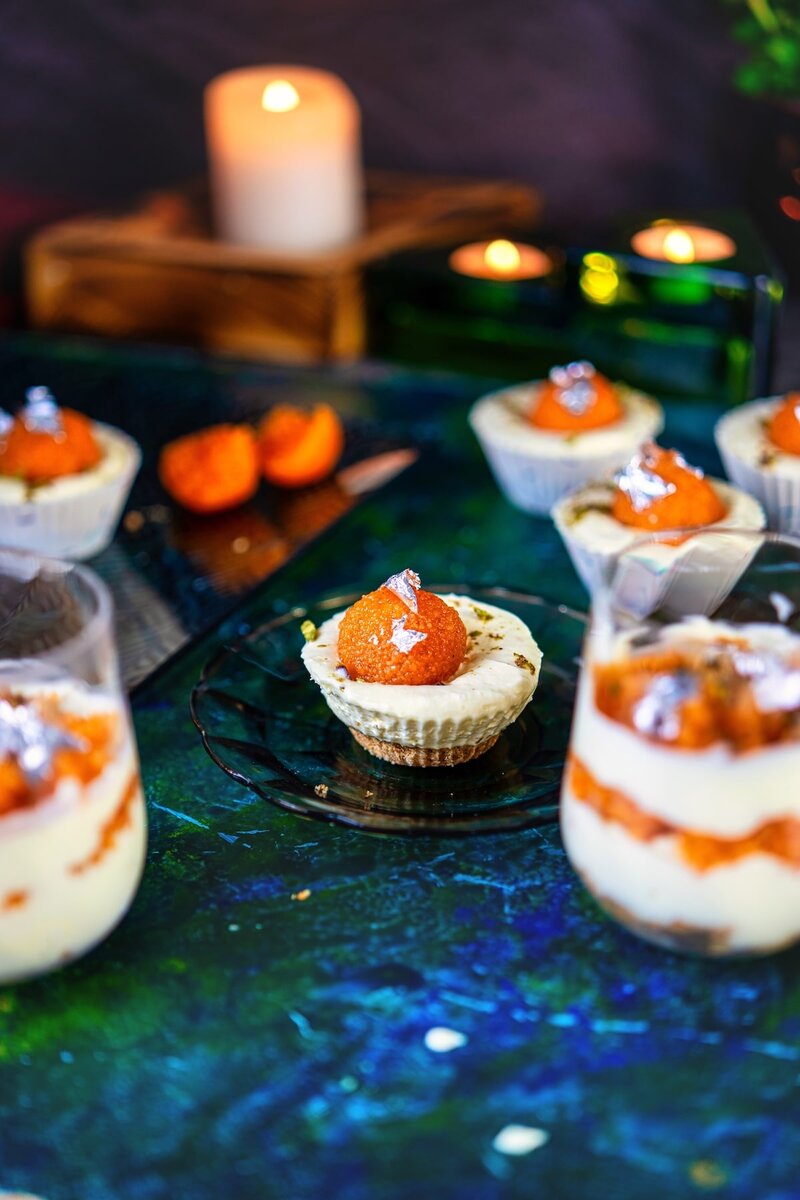 Assorted no bake motichoor cheesecakes and cheesecakes in glasses, adorned with motichoor ladoo and silver leaf, on a vibrant blue background