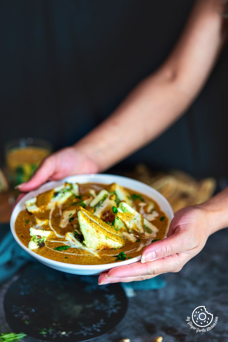 two hands holding pasanda served in a white ceramic bowl