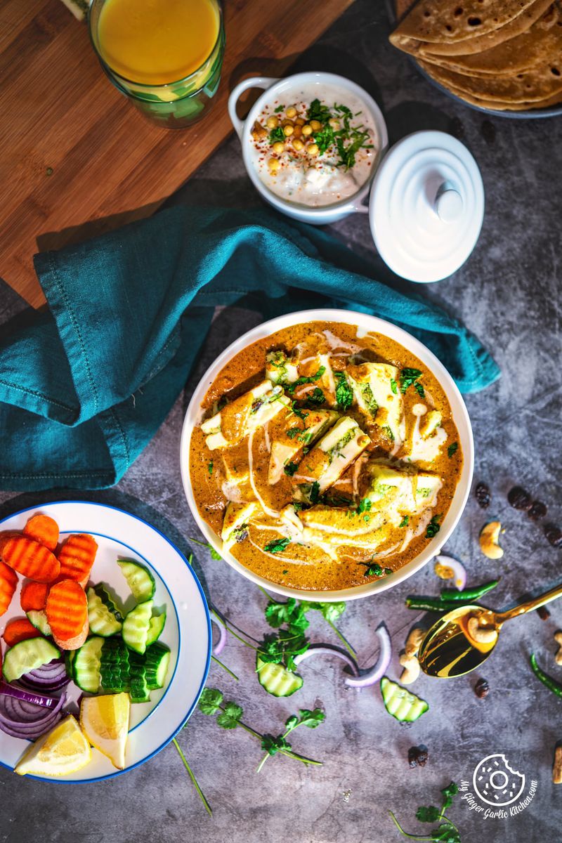 overhead shot of pasanda served in a white ceramic bowl with some salad and raita on the side