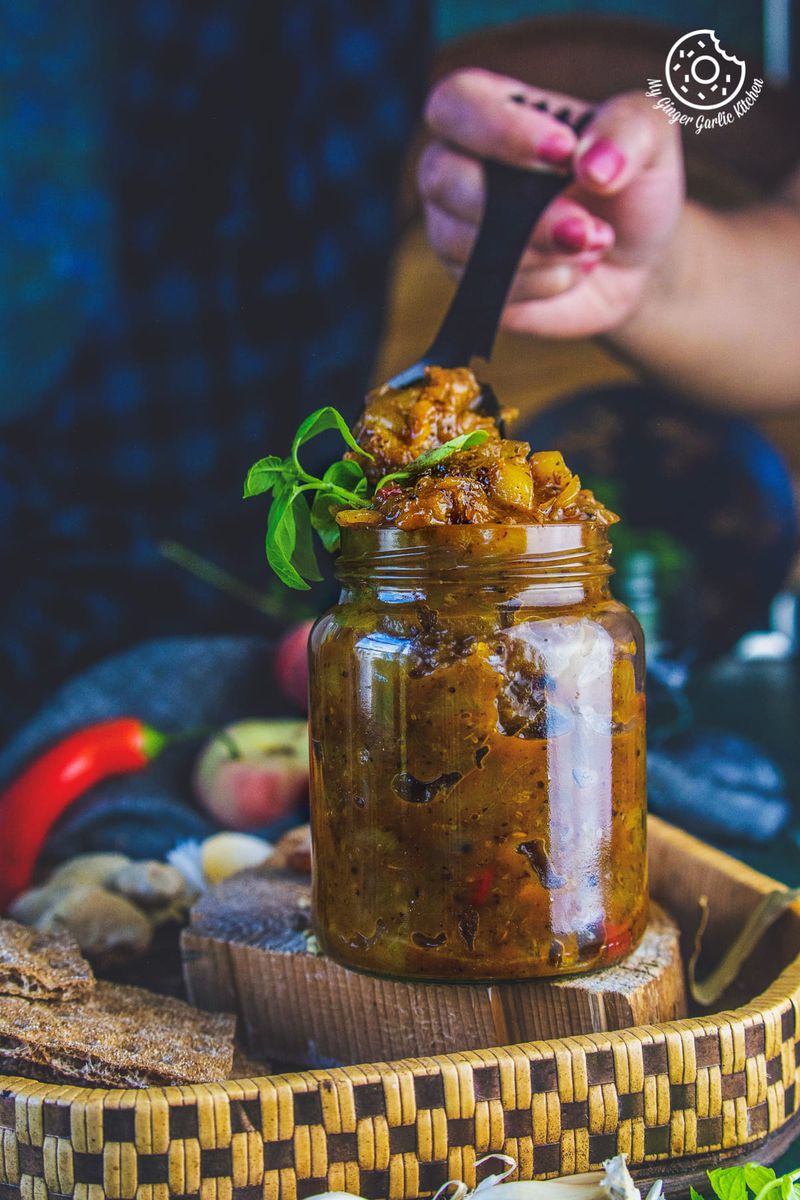 a female holding black metal spoon over peach chutney jar
