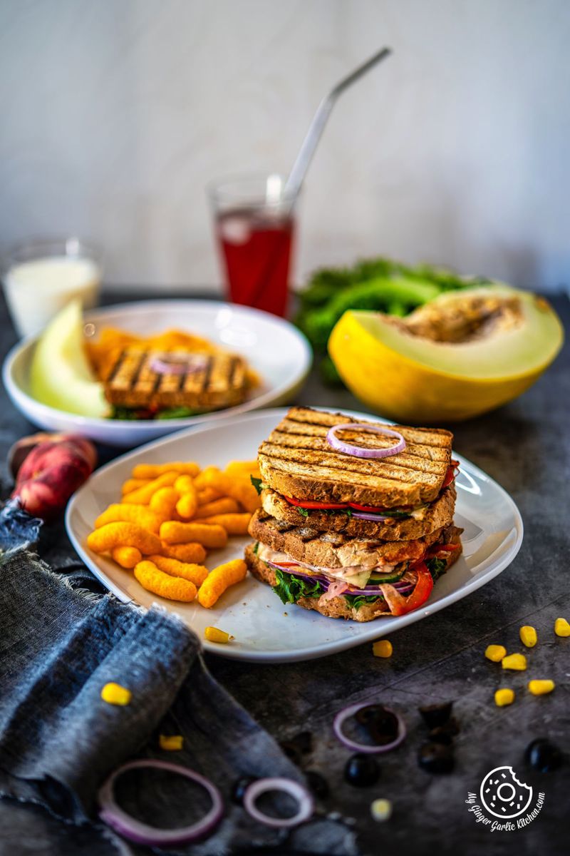 two peanut butter and veggie grilled cheese sandwiches in a white plate along with cheese puffs