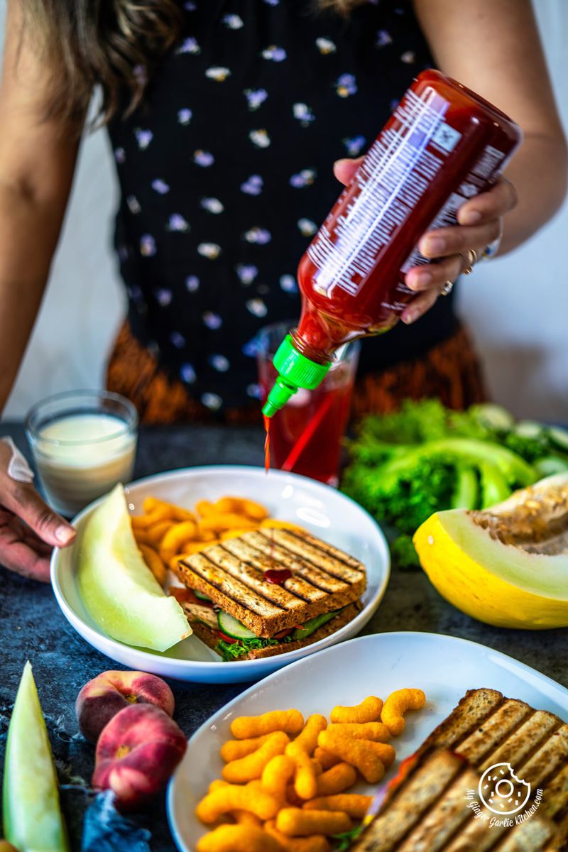 a female holding a ketchup bottle over a peanut butter and veggie grilled cheese sandwich