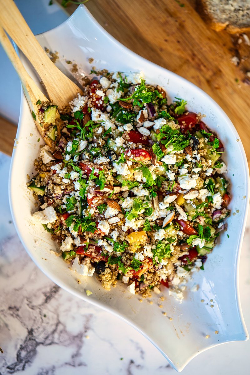A bowl of colorful quinoa salad with mixed vegetables, topped with crumbled feta cheese and fresh herbs.